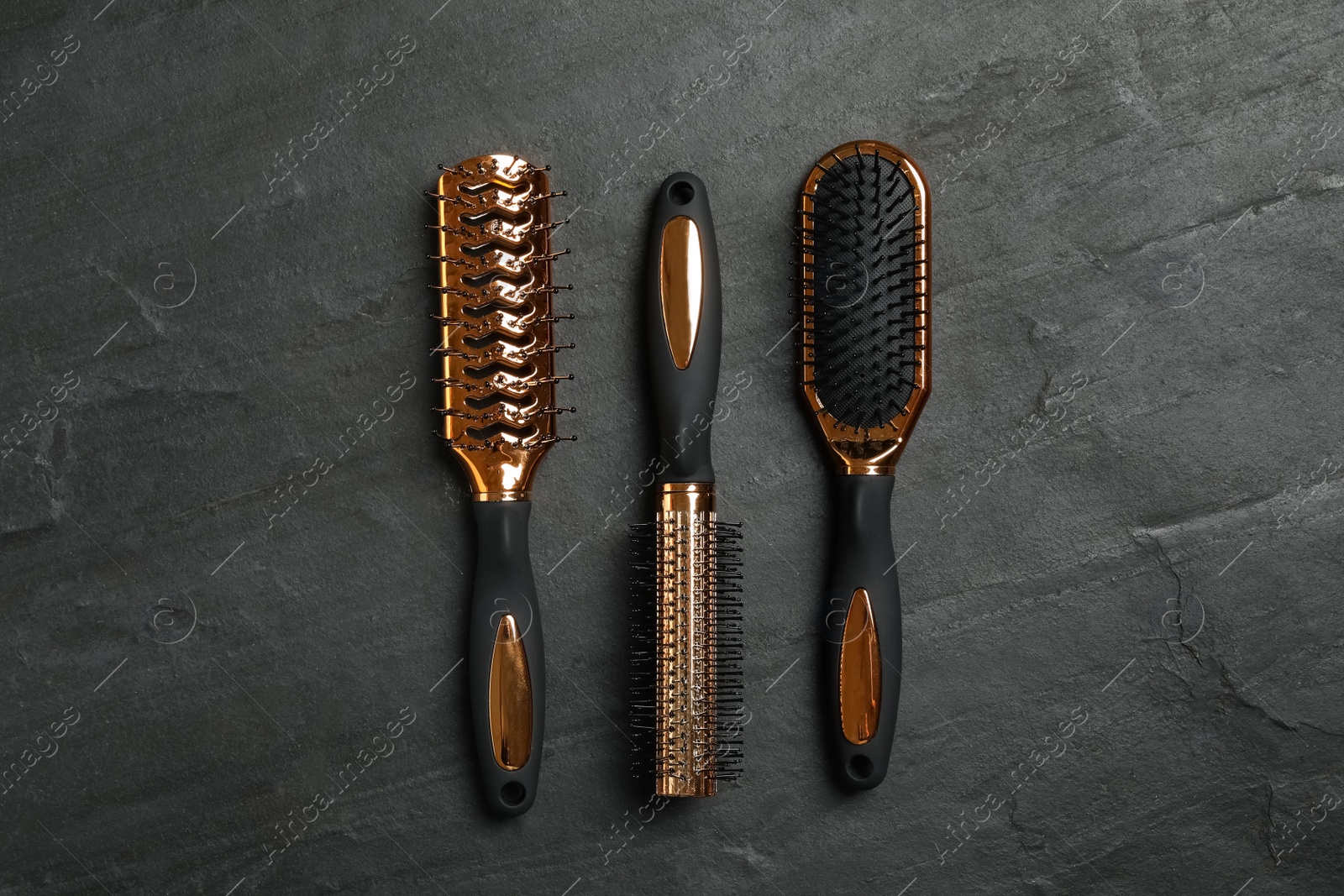 Photo of Set of hair brushes on black slate background, flat lay