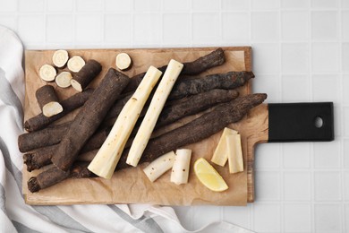 Photo of Raw salsify roots and lemon on white tiled table, top view