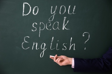 Photo of Teacher showing words Do You Speak English? written on green chalkboard, closeup