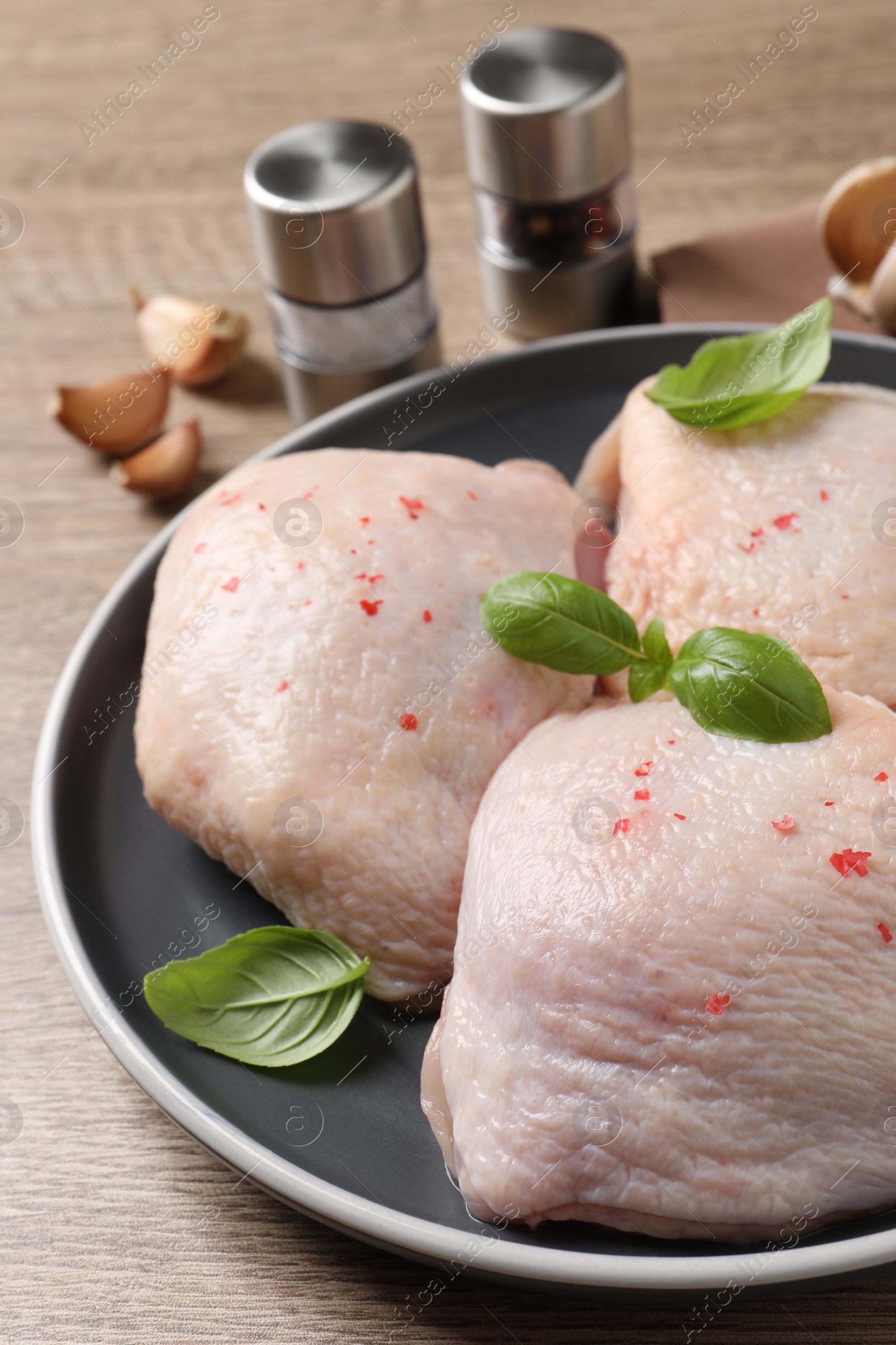 Photo of Raw chicken thighs with basil on wooden table, closeup
