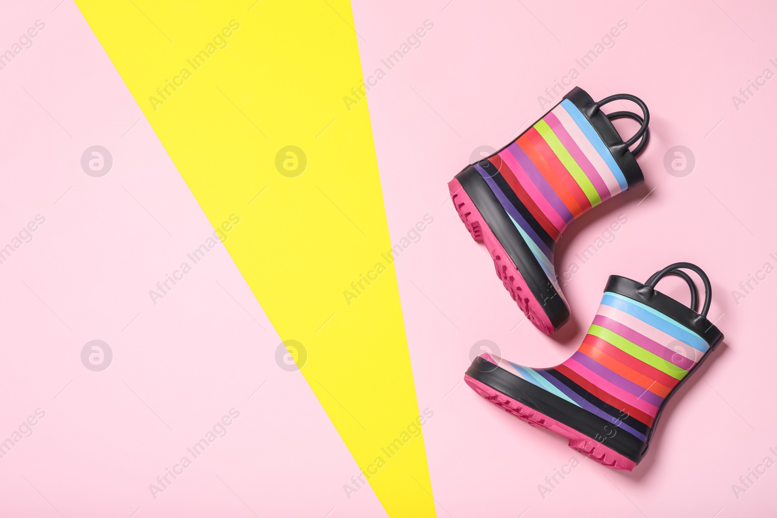 Photo of Pair of striped rubber boots on color background, top view. Space for text