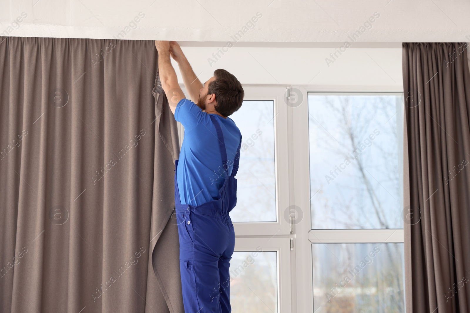 Photo of Worker in uniform hanging window curtain indoors