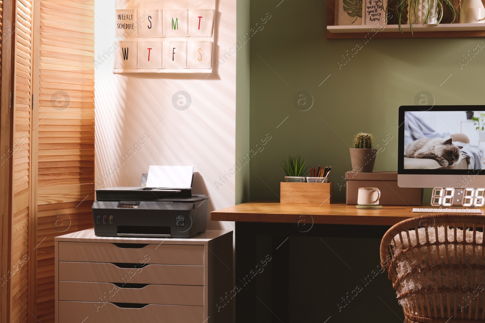 Photo of Stylish workplace with computer, printer and houseplant near olive wall at home