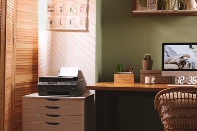 Photo of Stylish workplace with computer, printer and houseplant near olive wall at home