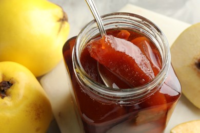 Taking tasty homemade quince jam from jar at table, closeup
