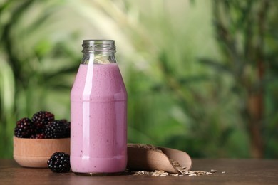 Photo of Delicious blackberry smoothie in glass bottle, oatmeal and berries on wooden table, space for text
