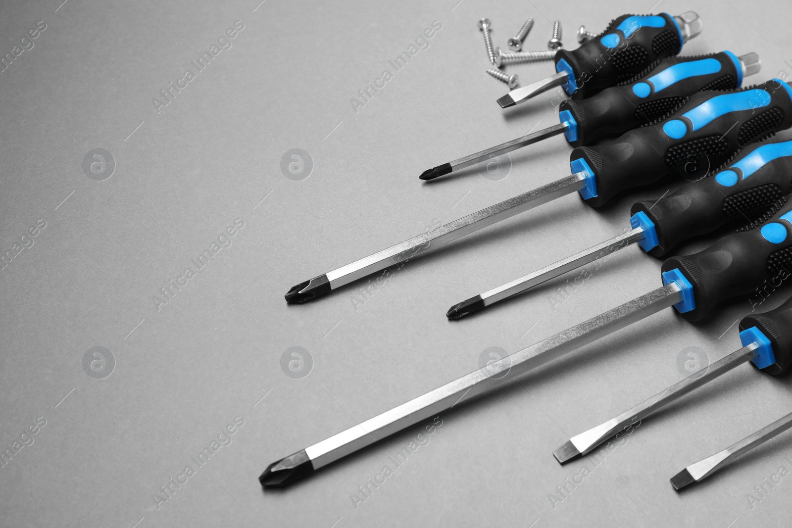 Photo of Set of screwdrivers and screws on grey background, space for text
