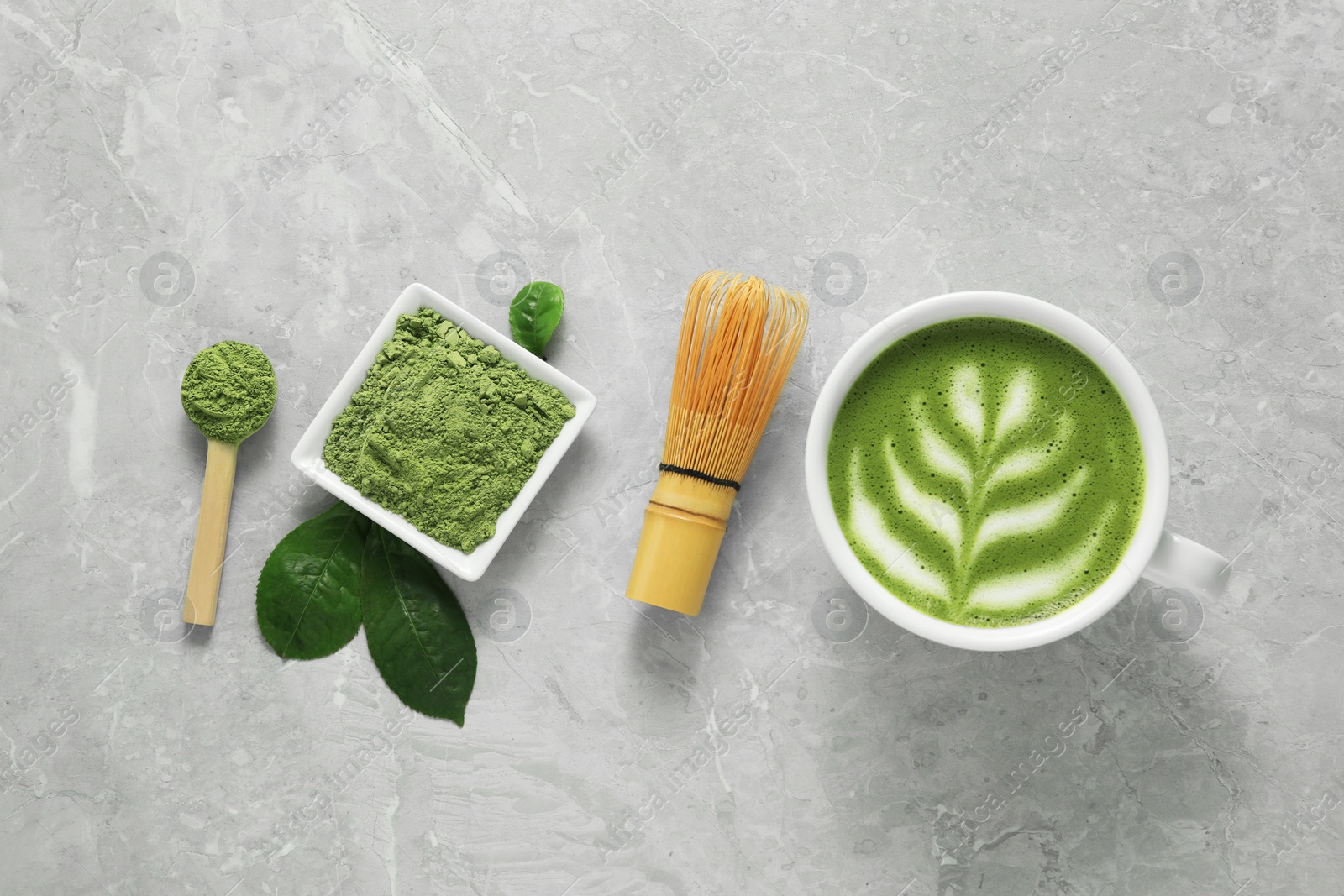 Photo of Cup of fresh matcha latte, powder and bamboo whisk on grey marble table, flat lay