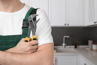 Image of Plumber with pipe wrench in kitchen, closeup. Space for text