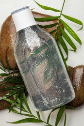 Bottle of micellar cleansing water, green twigs and spa stones on white table, flat lay