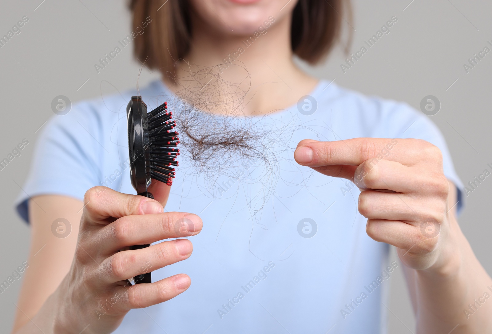 Photo of Woman taking her lost hair from brush on grey background, closeup. Alopecia problem