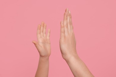 Photo of Mother and daughter giving high five on pink background, closeup of hands