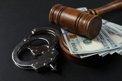 Photo of Judge's gavel, money and handcuffs on black background, closeup