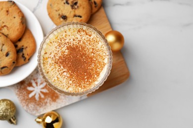 Photo of Glass of delicious eggnog with cinnamon and cookies on white table, flat lay. Space for text