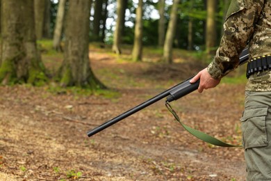 Photo of Man with hunting rifle wearing camouflage in forest, closeup. Space for text