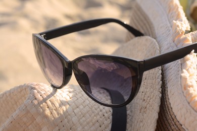 Photo of Hat with beautiful sunglasses on sandy beach, closeup