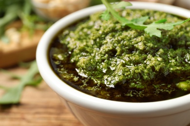 Photo of Bowl of tasty arugula pesto on table, closeup