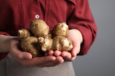 Photo of Woman holding Jerusalem artichokes on light grey background, closeup