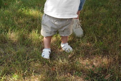 Mother supporting daughter while she learning to walk outdoors, closeup