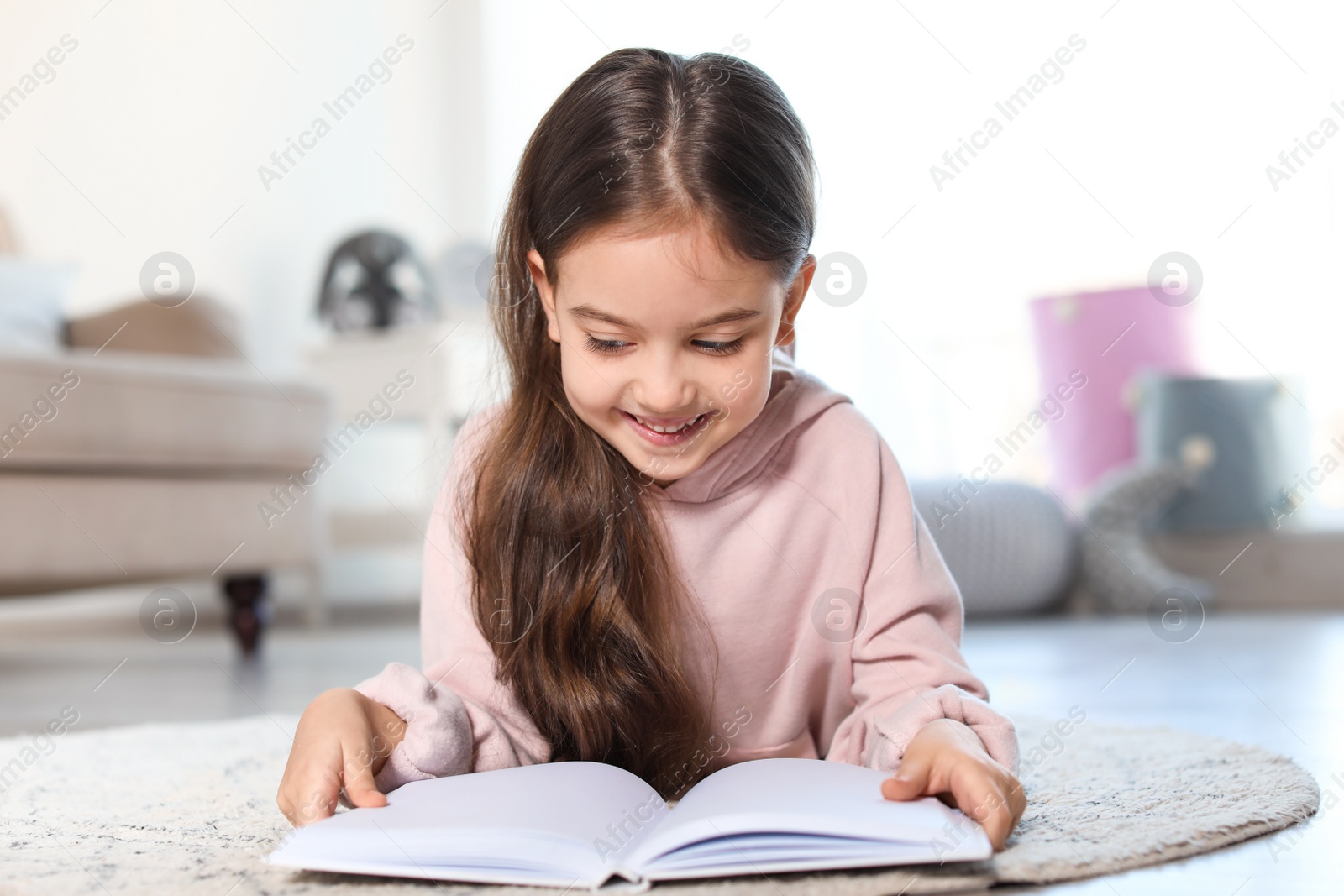 Photo of Cute child reading book on floor indoors