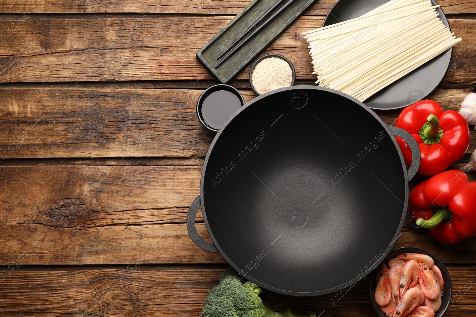 Photo of Empty iron wok and raw ingredients on wooden table, flat lay. Space for text