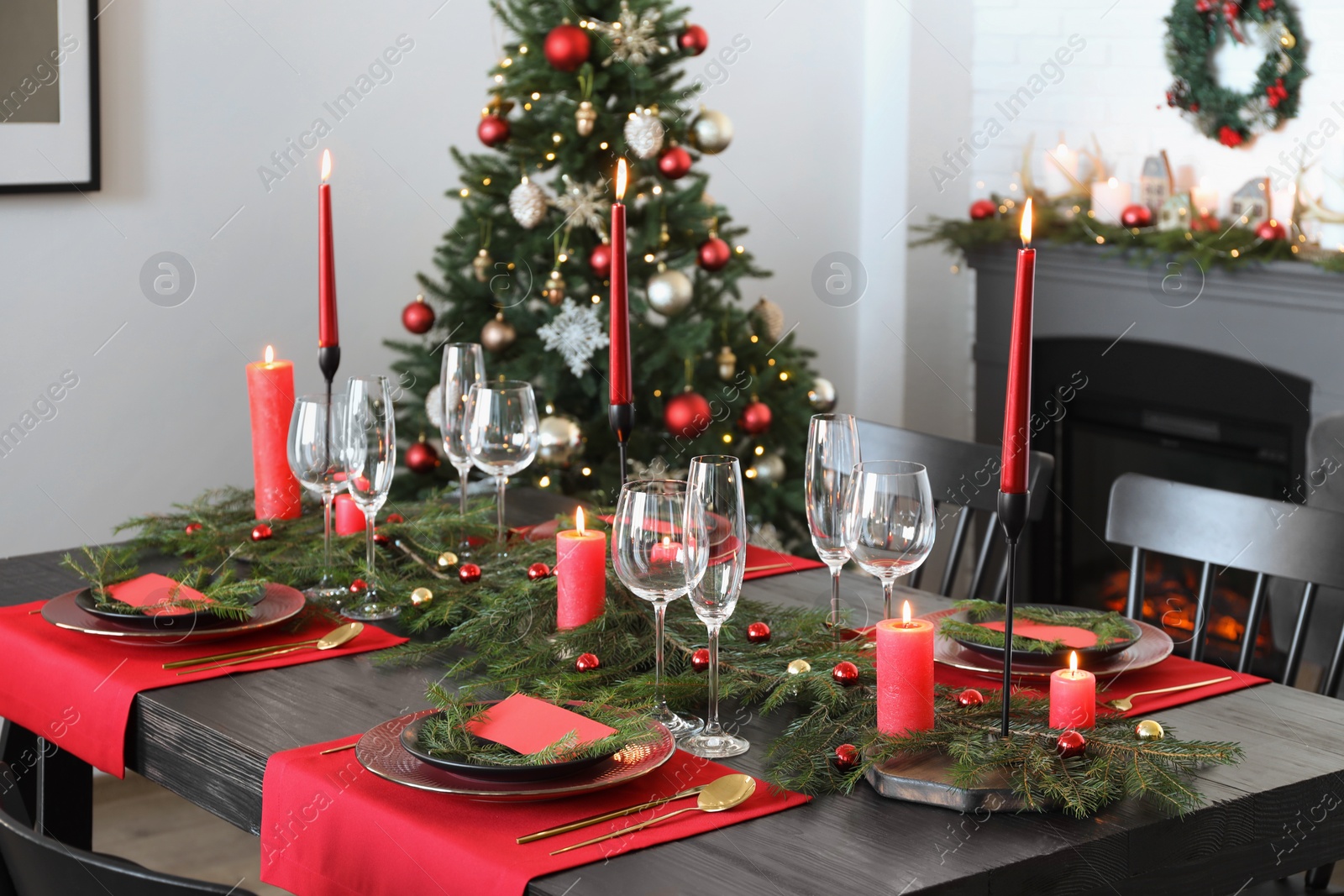 Photo of Elegant Christmas table setting with dishware and burning candles in festively decorated room