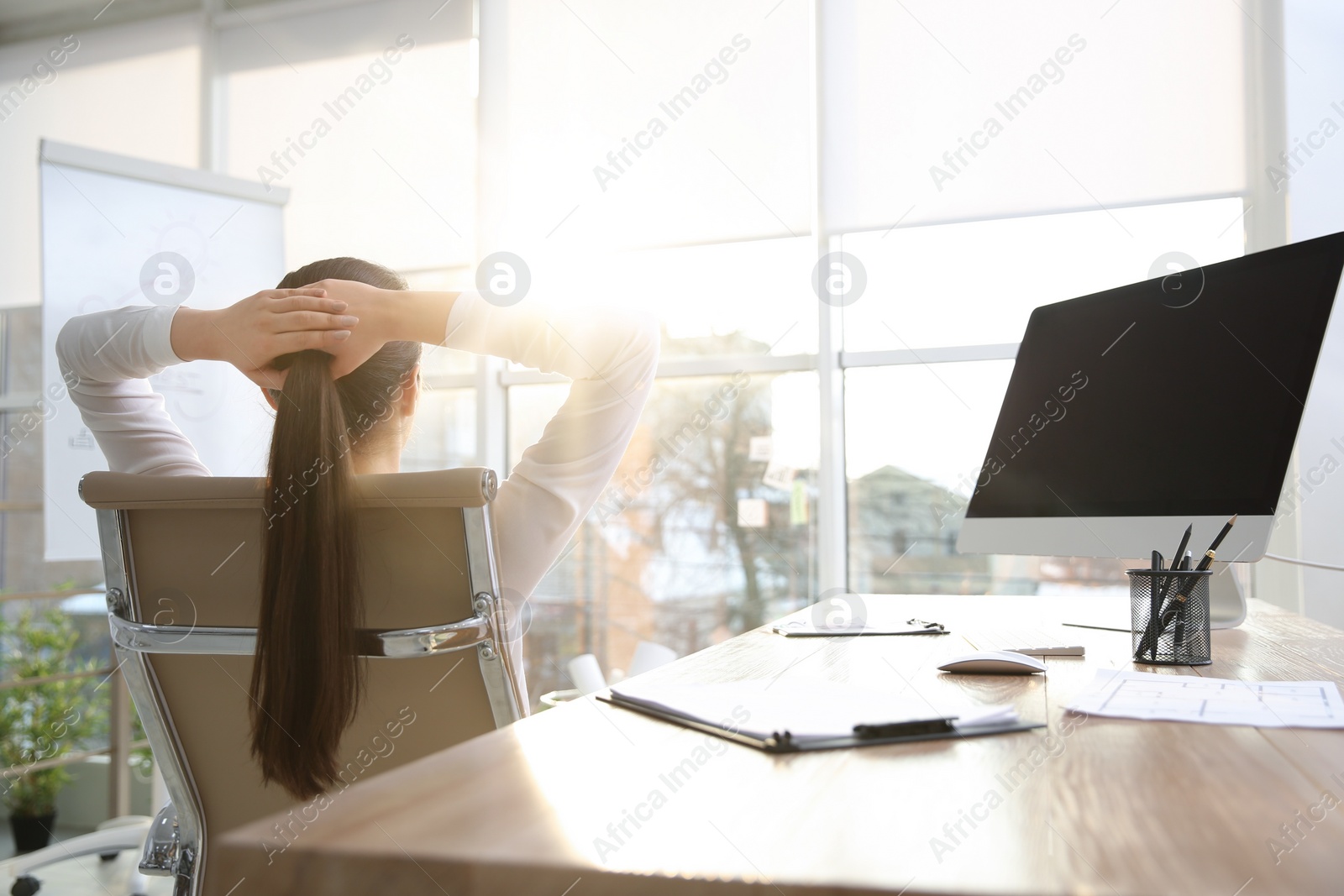 Photo of Young woman relaxing in office chair at workplace, back view