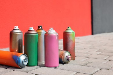 Photo of Cans of different spray paints on pavement near wall, space for text