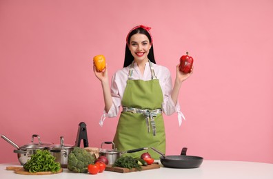 Photo of Young housewife with vegetables and different utensils on pink background