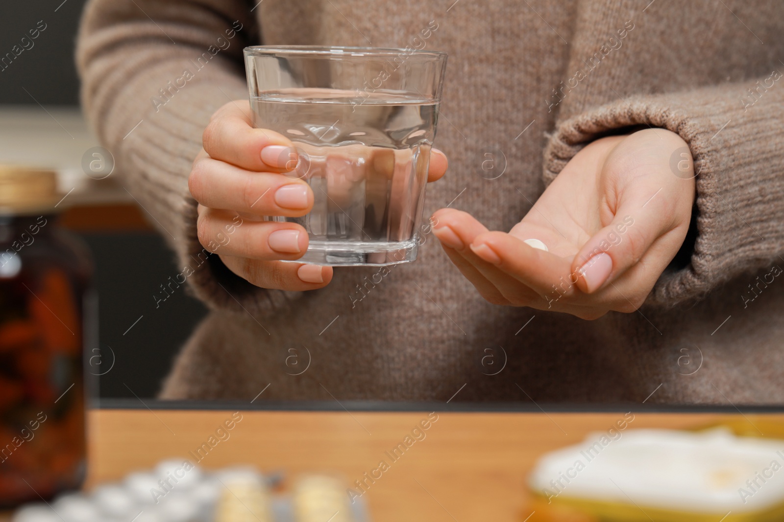 Photo of Woman with glass of water and pills at wooden table, closeup