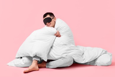 Photo of Happy man in pyjama and sleep mask wrapped in blanket on pink background