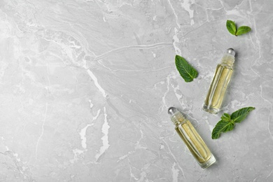 Glass bottles of essential oil, mint leaves and space for text on grey background, flat lay