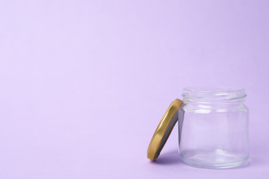 Open empty glass jar on lilac background, space for text