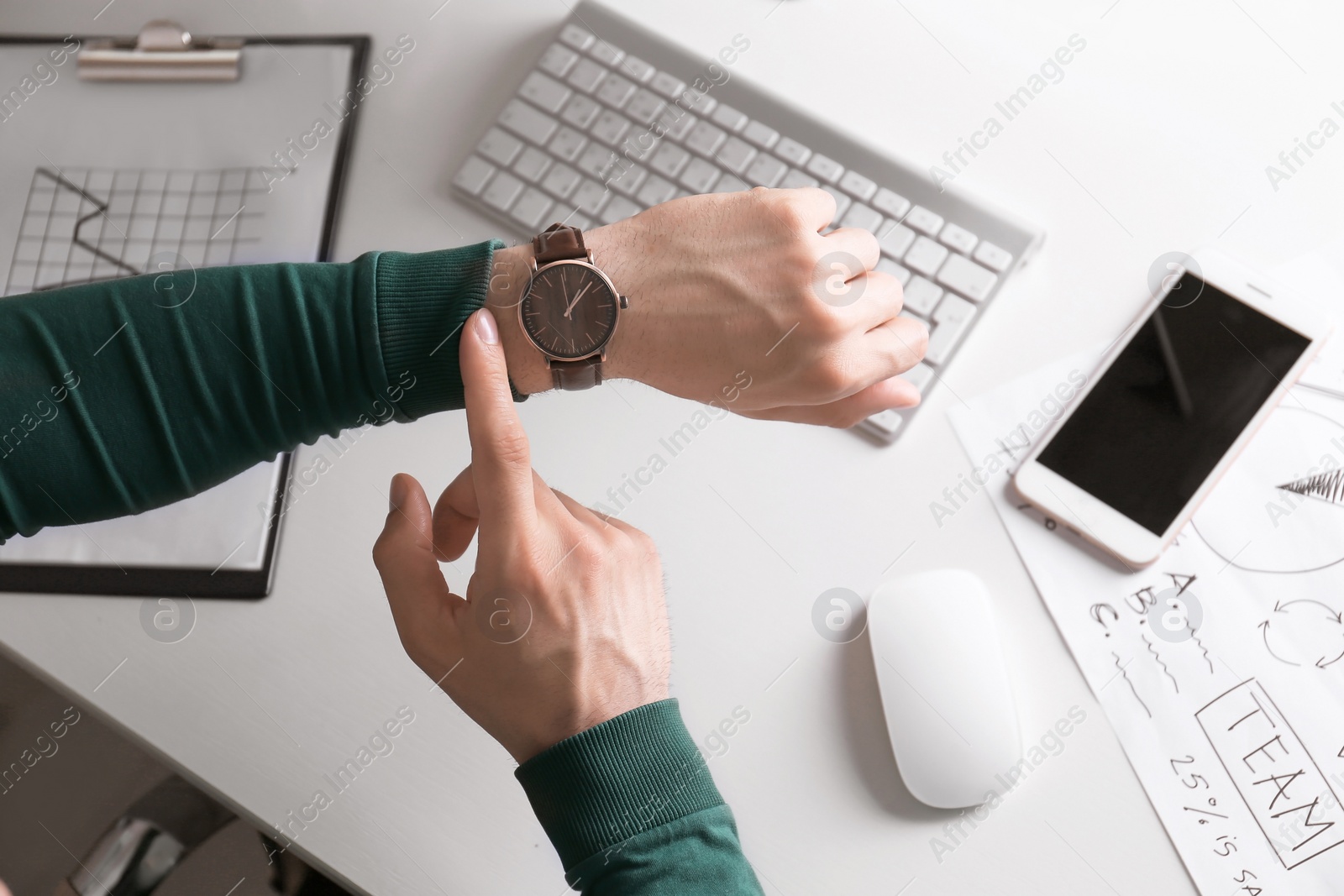 Photo of Young man checking time on his wristwatch at workplace