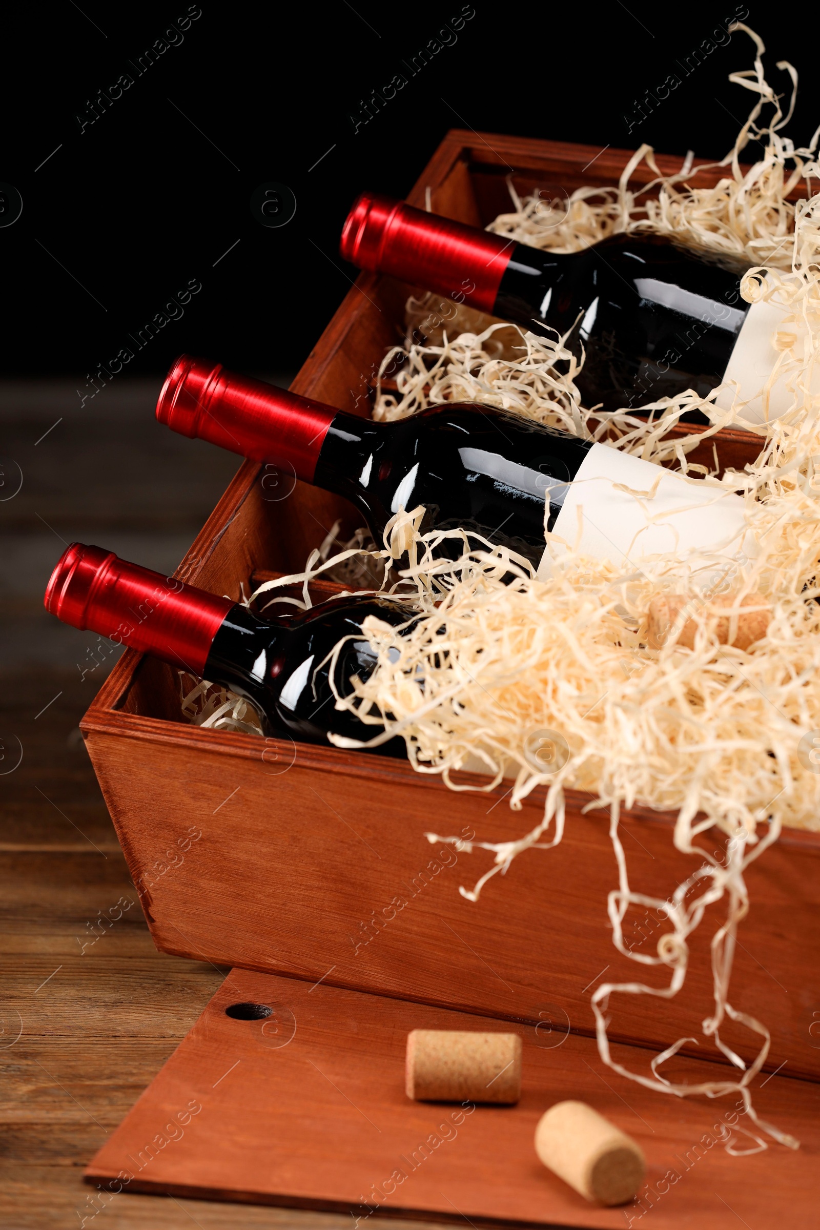 Photo of Box with wine bottles on wooden table against black background