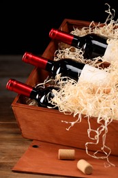 Photo of Box with wine bottles on wooden table against black background