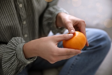 Photo of Woman with fresh tangerine on blurred background, closeup