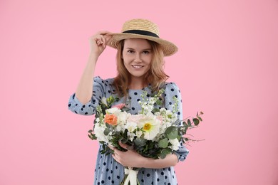 Beautiful woman in straw hat with bouquet of flowers on pink background