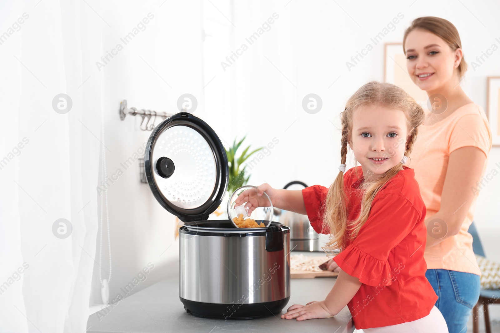 Photo of Mother and daughter preparing pasta with modern multi cooker in kitchen