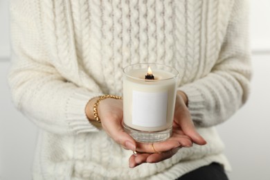 Photo of Woman with stylish jewelry holding burning soy candle on light background, closeup