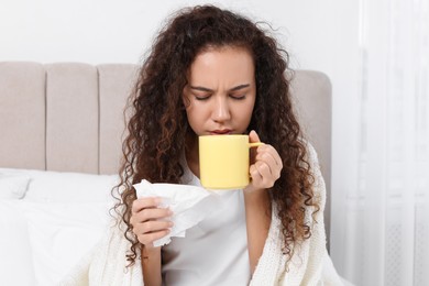 Photo of Sick African American woman with tissue and cup of drink in bed at home