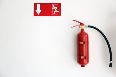Photo of Fire extinguisher and emergency exit sign on white wall, space for text