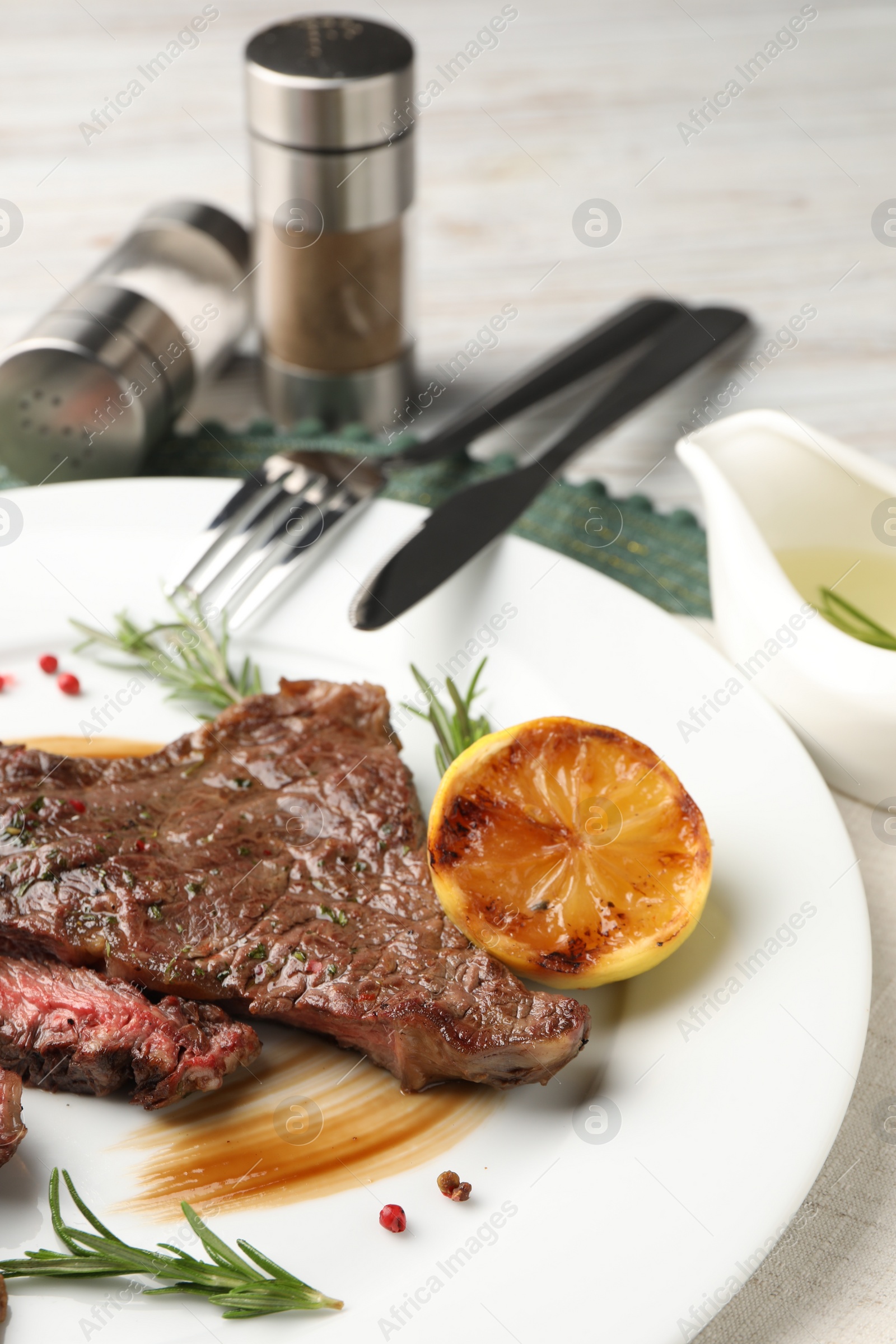 Photo of Delicious grilled beef steak with spices and lemon served on table, closeup