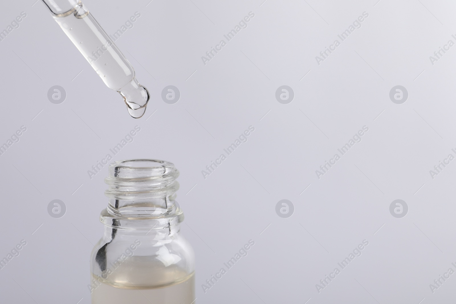 Photo of Dripping cosmetic serum from pipette into bottle on light grey background, space for text