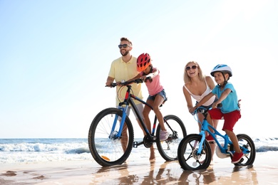 Photo of Happy parents teaching children to ride bicycles on sandy beach near sea