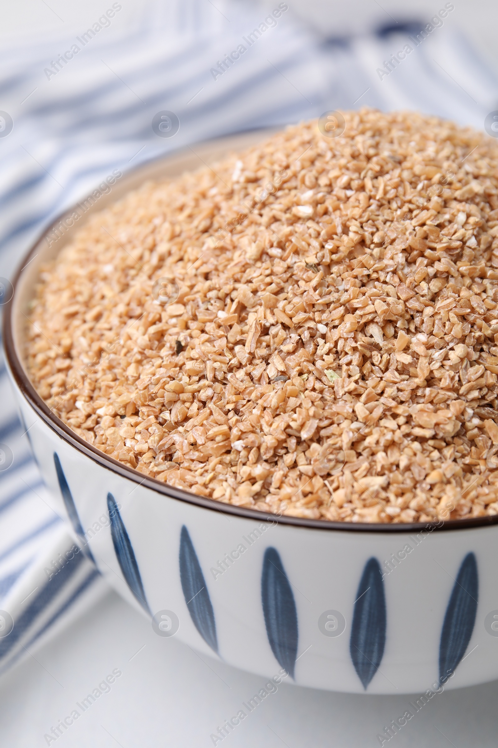 Photo of Dry wheat groats in bowl on white table, closeup