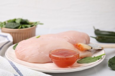 Photo of Marinade, basting brush and raw chicken fillets on white table, closeup
