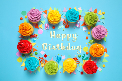 Image of Delicious cupcakes and text Happy Birthday on light blue background, flat lay