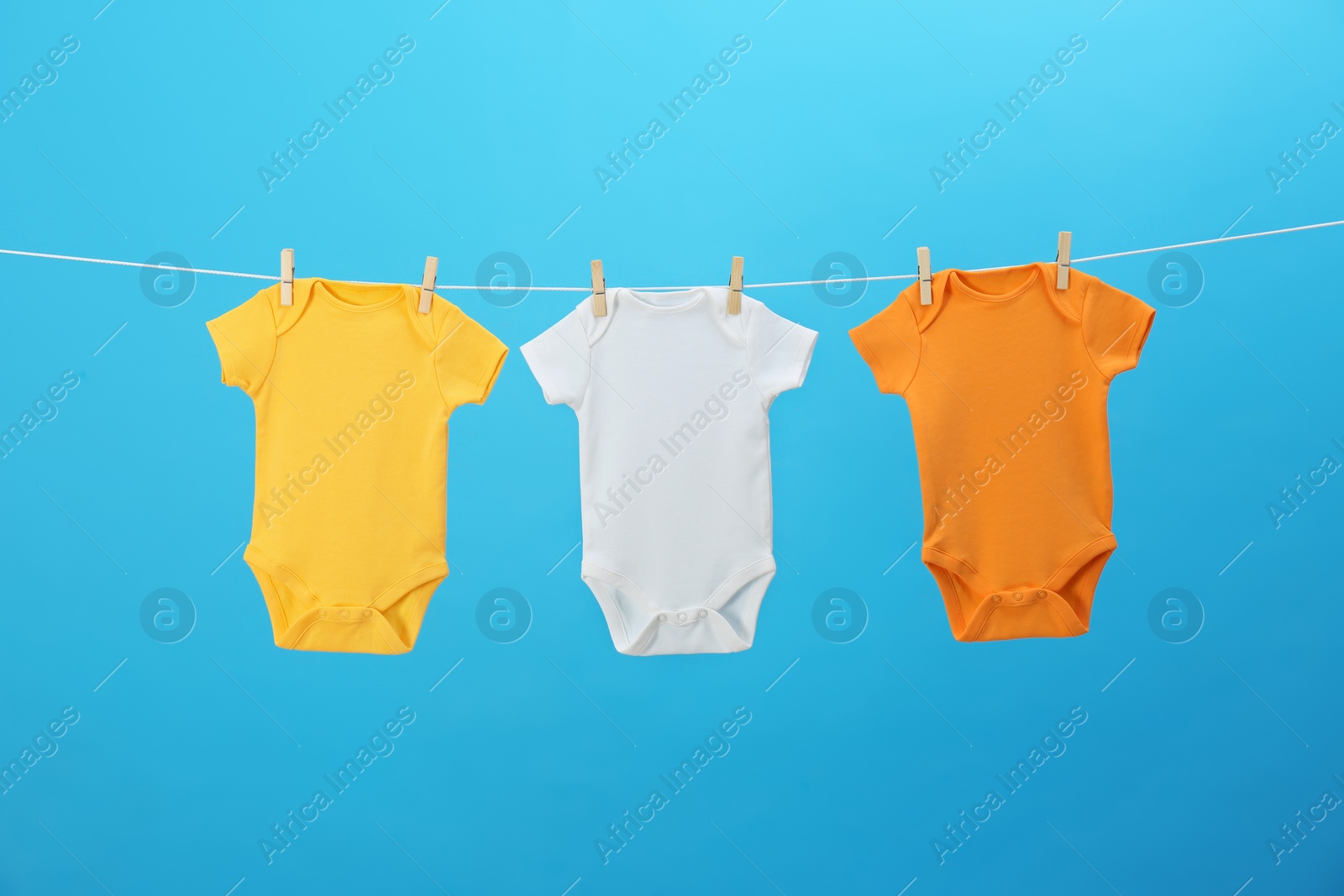 Photo of Colorful baby onesies hanging on clothes line against blue background. Laundry day