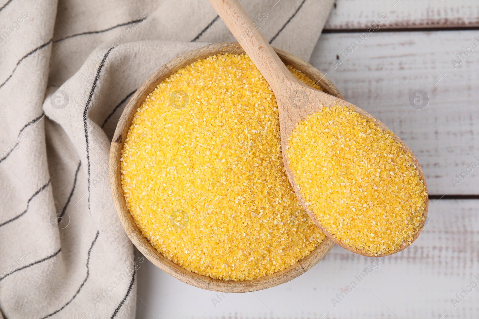 Photo of Raw cornmeal in bowl and spoon on light wooden table, top view